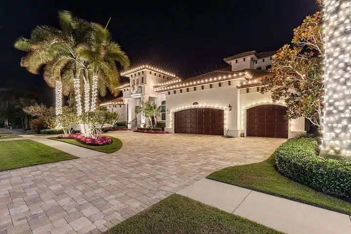 Christmas lights outlining the roofline and wrapped up the palm trunks of a two-story home at night